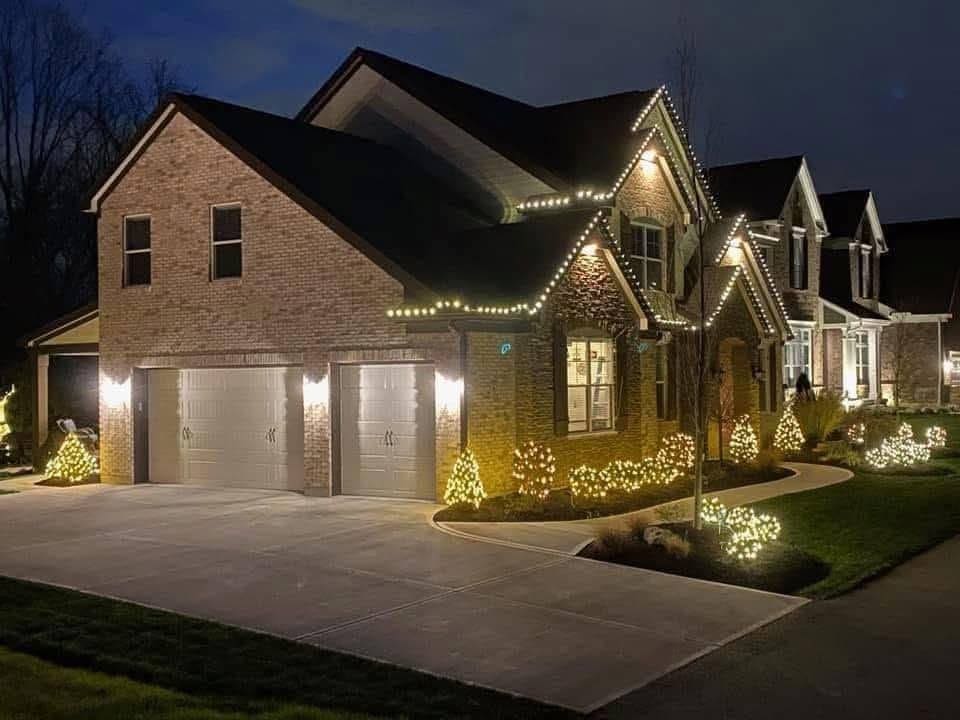 Brick home with the roofline lit and wrapped trees along the driveway